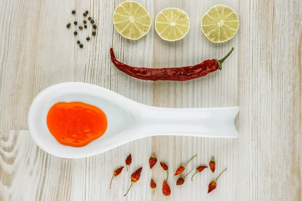 food harmful to sick people - spicy chili sauce in a ceramic spoon with a variety of spices: chili peppers, black pepper, chilli, lime on white wooden table