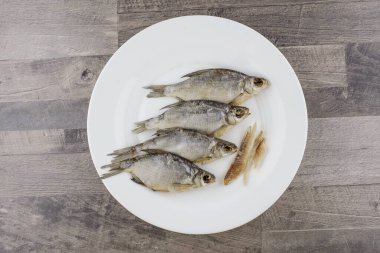 bira aperatifi: beyaz tabakta 4 güneşte kurutulmuş tatlı su balığı - vitamin ve protein kaynağı, soyulmuş birkaç et parçası, gri masa, merkezi konum
