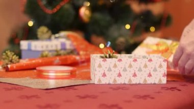 Büyükannesinin Noel ve Yeni Yıl için torununa hediye paketlemesinin yavaş çekimleri. Noel ve yeni yıl tatili hazırlığı kavramı, Noel ağacı geçmişi.