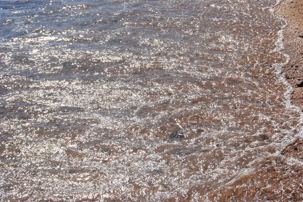 Волны и прозрачная вода на песке на пляже. Текстура. Пена для воды. Солнечный день — стоковое фото