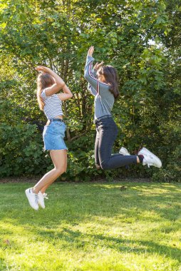 Kızlar zıplıyor. Hayatta mutlu bir an ve mükemmel bir an ve yer. Genç arkadaşlar parkta eğleniyor. Çeşitlilik. Dostluk.
