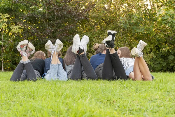 Beeld van de benen en schoenen van jonge tieners meisjes staan op het gras van een park. Genieten van een gelukkig moment en een perfecte plek. Plezier hebben en genieten van hun vriendschap. Concept van eenheid en diversiteit. — Stockfoto