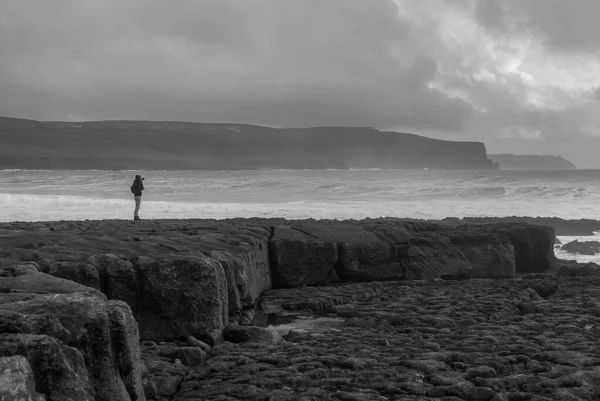 Silueta mladé ženy v Doolin, County Clare, Irsko, s útesy v pozadí. Zatažené nebe při západu slunce. Velké skály v popředí. Divoký Atlantik. V černé a bílé — Stock fotografie