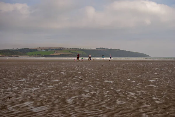 Οι άνθρωποι περπατούν στην αμμώδη παραλία. Οικογένεια με παιδιά και ένα σκυλί που περπατά και παίζει στην παραλία Kilbrittain, Ιρλανδία. Απολαμβάνω τη μέρα. Συννεφιά. — Φωτογραφία Αρχείου
