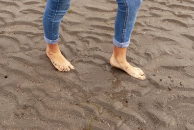 Kumsalda yürüyen bir kadın sahilde ayak izleri bırakıyor..