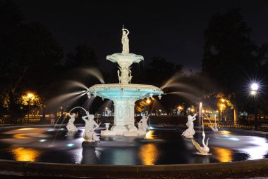 Savannah, Ga- Mart 24, 2014: Forsyth Çeşmesi ağaçların içinden geç güneş filtreleri ve çeşme heykelleri ışıklı olarak akşam fotoğraflandı, Forsyth Park, Savannah, Ga