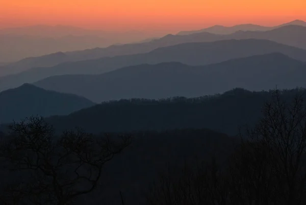Mountain ranges which appear gray at sunrise are viewed against an orange sky at Great Smoky Mountains National Park.