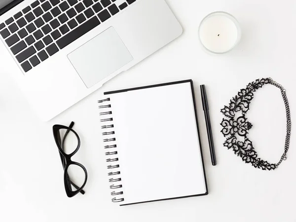 Laptop, eyeglasses, candle, necklace notepad and pen.