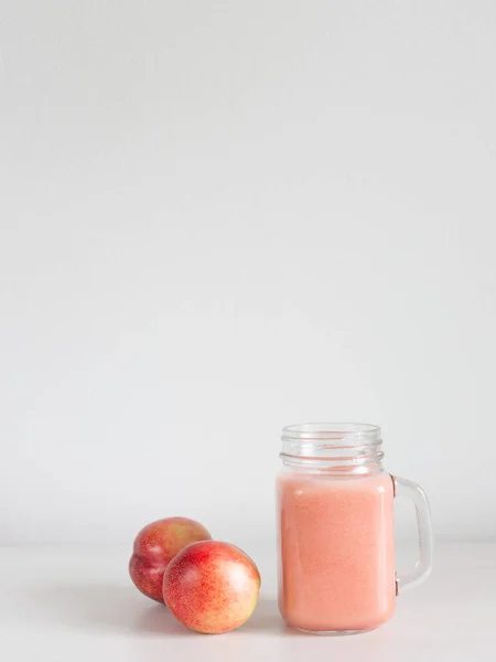 Un frasco de vidrio con batido rosa y dos melocotones de nectarina — Foto de Stock