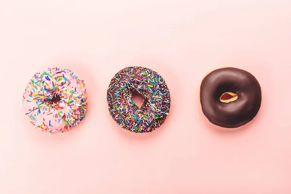 Three tasty doughnuts on pink background.