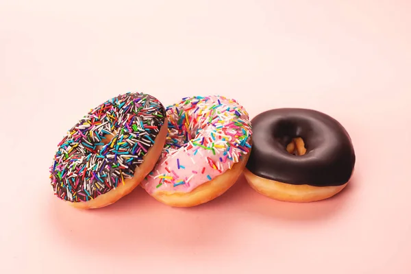 Three tasty doughnuts on pink background.