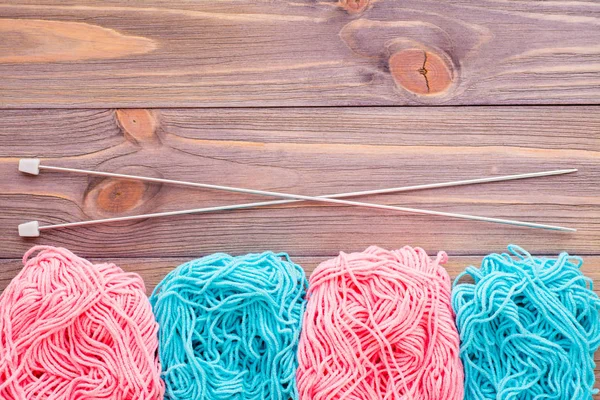 Tangles of pink and mint yarn and needles on a wooden background. Top view