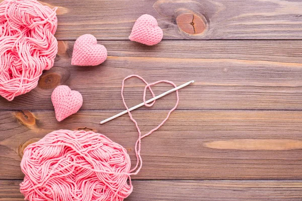 Knitted pink hearts, tangle of thread and needle on a wooden background. Top view
