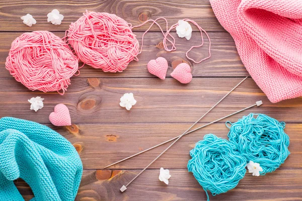 Tangles of pink and mint yarn, snuds, needles and knitting hearts on a wooden background. Top view