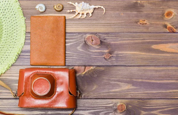 Camera in a case, passport, hat and seashells on a wooden background. Retro style. Place for the inscription. Vacation concept.