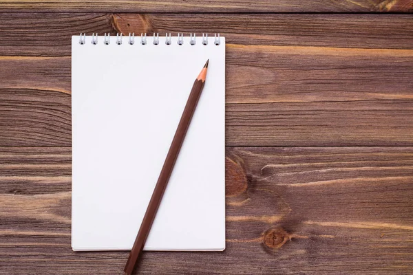 Clean open notepad for writing on a spiral mount sheet and brown pencil on a wooden background. Top view. Copy space