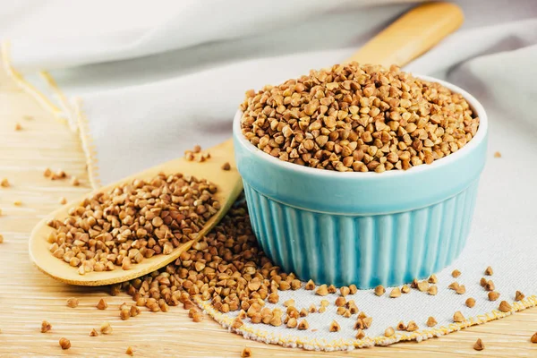 Raw buckwheat grains in a bowl and in a wooden spoon on the table