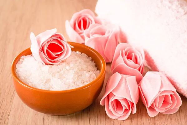 Soap in the form of flowers, sea salt in the bowl and towel on a wooden background