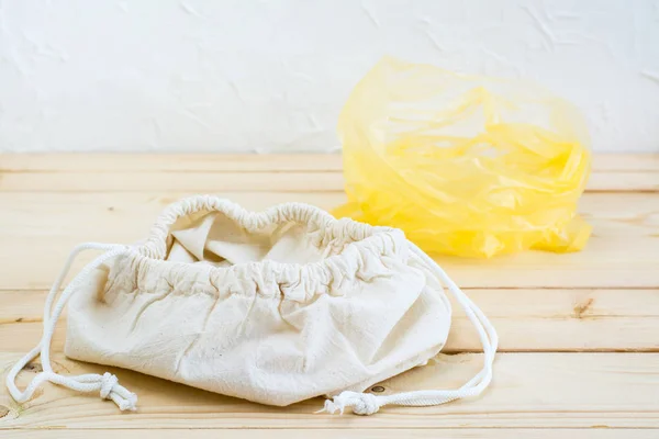 An empty opened canvas bag with ties for food and a plastic bag on a natural wooden background