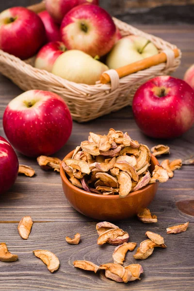 Sliced dried apples in a bowl and fresh apples on a wooden table