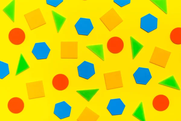 Various flat figures - circles, triangles, squares, hexagons - lie abstractly on yellow cardboard
