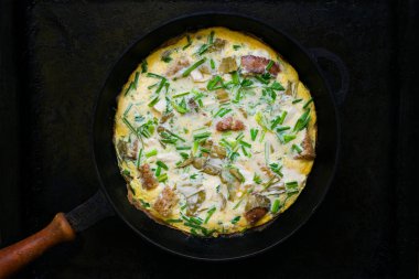 Otlar, ekmek, et, soğan ve sarımsak karanlık bir arka plan üzerinde bir tavada omlet. Düşük anahtar. Seçici odak. Üstten görünüm