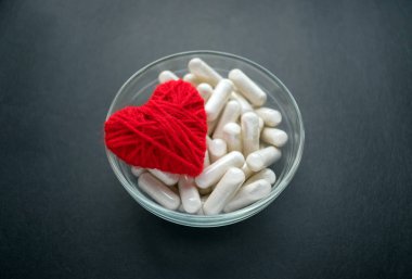 White veg capsules and red thread heart in glass bowl on black background. Anticoagulant, Blood Thinners. Cardiac Medications, pills for the heart. Treat Heart disease Failure clipart