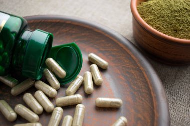 Yeşil kapsül, şişe ve toz bir çuval bezi arka planda bir kil kahverengi tabakta kapatın. Kilo kaybı ve detoks diyet takviyeleri. Vitaminler ve mineraller vegans ve vejetaryenler için. Superfood