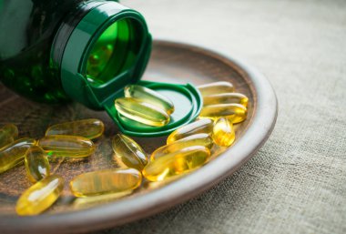 Sarı D3 vitamini (cholecalciferol) jelatin kapsül ve kil plaka çuval bezi zemin üzerine yeşil şişe. D3 vitamini (cholecalciferol) besin kemik sağlığı desteklemek için faydalı