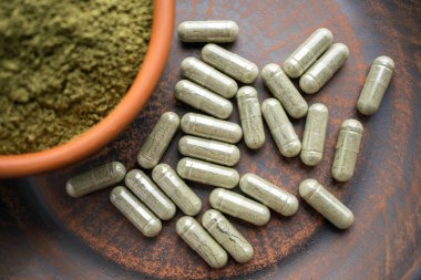 Yeşil kapsül ve toz bir çuval bezi rustik arka planda bir kil kahverengi tabakta kapatın. Diyet takviyeleri, vitaminler ve mineraller vegans ve vejetaryenler için. Sağlıklı yaşam, superfood