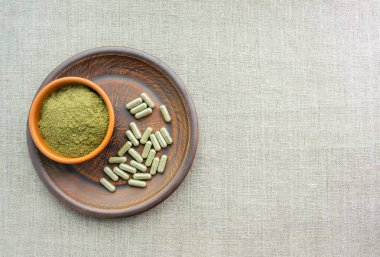 Kratom yeşil kapsül ve toz kahverengi plaka üzerinde ek. Bitkisel ürün alt-tıp kratom opioid. Ev alternatif ağrı ilaç, opioid bağımlılığı, tehlikeli ağrı kesici, aşırı doz. Kopya alanı