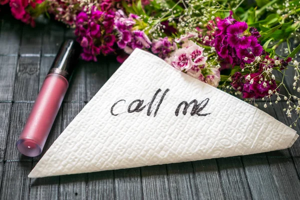 The inscription CALL ME on a white napkin left on the table in a cafe. Text call me on a background of pink flowers and lipstick. Dating, Love meeting