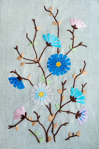 美丽的手工刺绣的粉红色和蓝色的花朵和芽 棕色茎和绿色的叶子在灰色亚麻织物的背景 花细腻刺绣缎缝 — 图库照片