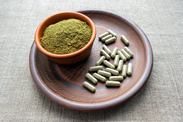 Green capsules and powder on a clay brown plate on a burlap rustic background. Dietary supplements, vitamins and minerals for vegans and vegetarians. Healthy lifestyle, superfood