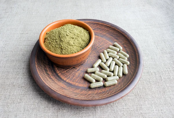 Kratom yeşil kapsül ve toz kahverengi plaka üzerinde ek. Bitkisel ürün alt-tıp kratom opioid. Ev alternatif ağrı ilaç, opioid bağımlılığı, tehlikeli ağrı kesici, aşırı doz. Yakın çekim