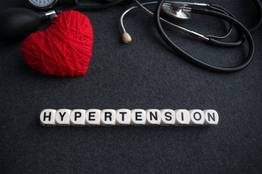 Word kalp hipertansiyon harflerle kırmızı iplik kalp ve tonometer koyu arka plan üzerinde beyaz küpleri. yüksek tansiyon yazıt ile tıbbi malzeme için kalp diagnostics, stetoskop 