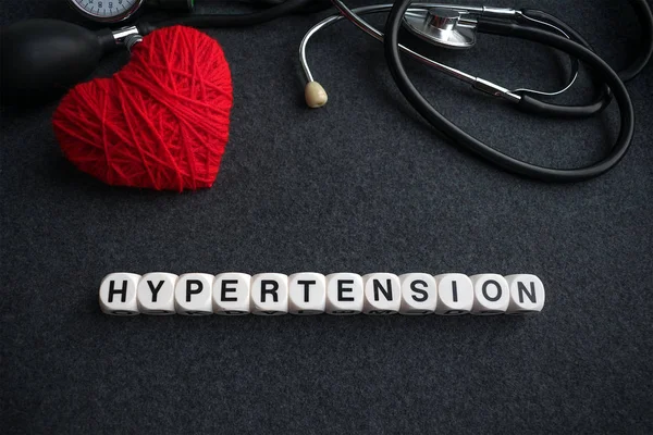 Word kalp hipertansiyon harflerle kırmızı iplik kalp ve tonometer koyu arka plan üzerinde beyaz küpleri. yüksek tansiyon yazıt ile tıbbi malzeme için kalp diagnostics, stetoskop 