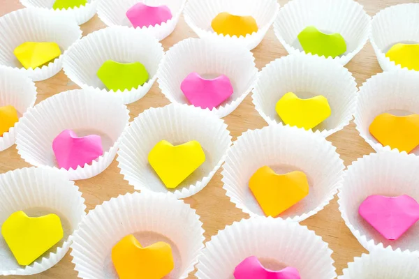 A lot of paper colorful origami heart in round white cupcake molds. Modern bright romantic background. Origami paper hearts geometric volume. Colored paper heart.