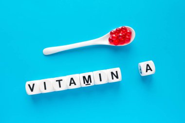 Kırmızı kapsül beyaz kaşık ve mavi bir arka plan üzerinde beyaz küpleri harflerle A vitamini kelime. sağlıklı ve tıbbi kavramı. Retinol, Retina, retinoik asit, provitamin A, karotenoid, beta-karoten sağlık yararları