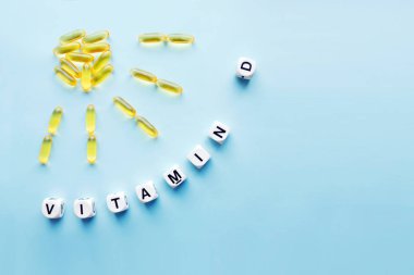 Güneş ışınları ve mavi bir arka plan üzerinde beyaz küpleri harflerle D vitamini word ile şeklinde sarı kapsül. Sağlıklı ve tıbbi kavramı için D vitamini kelime. Işığı vitamini sağlık yararları