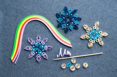 Paper quilling Christmas Crafts in the form of snowflakes from strips of paper. Tools and materials for Christmas quilling diy on a gray felt background. The process of creating Christmas decorations from paper clipart