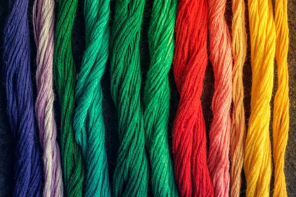 Parlak renkli nakış iplikçikleri. Koyu renk keçeli kumaş üzerine işlenmiş çok renkli iplikler. El yapımı nakış işleme arka planı