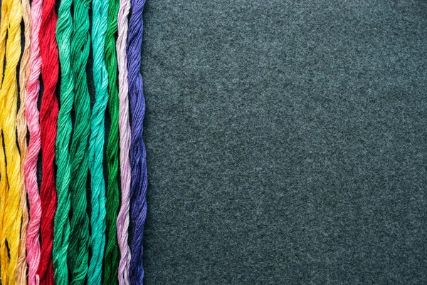 Bright multicolored embroidery thread yarns. Skeins of multicolored embroidery threads on dark felt canvas. Handmade embroidery sewing background