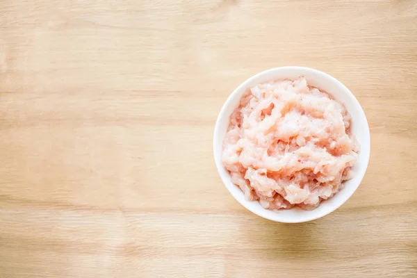 Raw meat. Fresh chicken minced meat in a round white plate on a wooden background. Dietary meat, low-calorie foods, an ingredient for chicken dishe