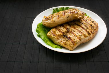 Tavuk yaprakları kayrak siyah bir ahşap zemin üzerine beyaz yuvarlak tabakta biftek ızgara. Sağlıklı gıda. Diyet, fitness gıda. B-B-Q.