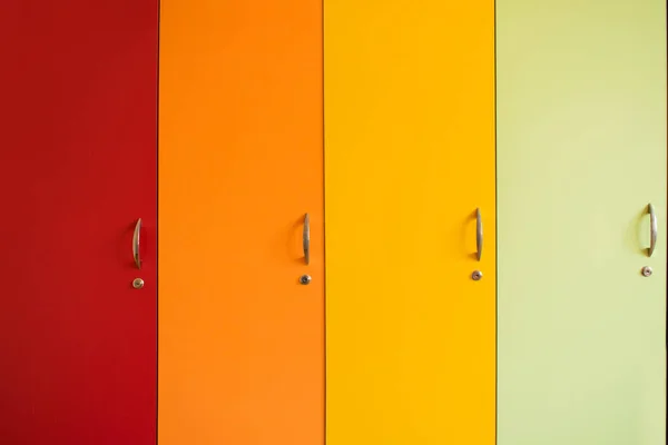 Colorful bright doors of cabinets with handles. Rainbow furniture in kindergarten or school. Bright background of yellow orange, red and green