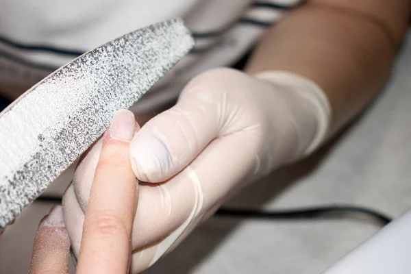 Process manicure close-up. Preparation for hardware manicure. Beautician  in rubber gloves handles the nail of the client with a nail file. Selective focus on costumer\'s finger