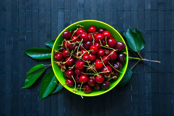 Taze organik kiraz meyveleri koyu rustik ahşap arka plan üzerinde parlak yeşil kase