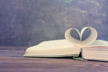 Koyu ahşap masa üzerinde açık kitap kalp şeklinde kağıt sayfadan. Aşk, Romantik, dating, aşk hikayesi, mutlu sevgililer günü kavramı kopya alanı ile. Seçici odak