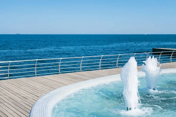 The gush of water of fountain. Splash and Foam of water. Blue vertical fountain with mosaic pool on the wooden terrace, by the sea. Rest on the beach, sea freshness in the summer heat. Siesta on the beach
